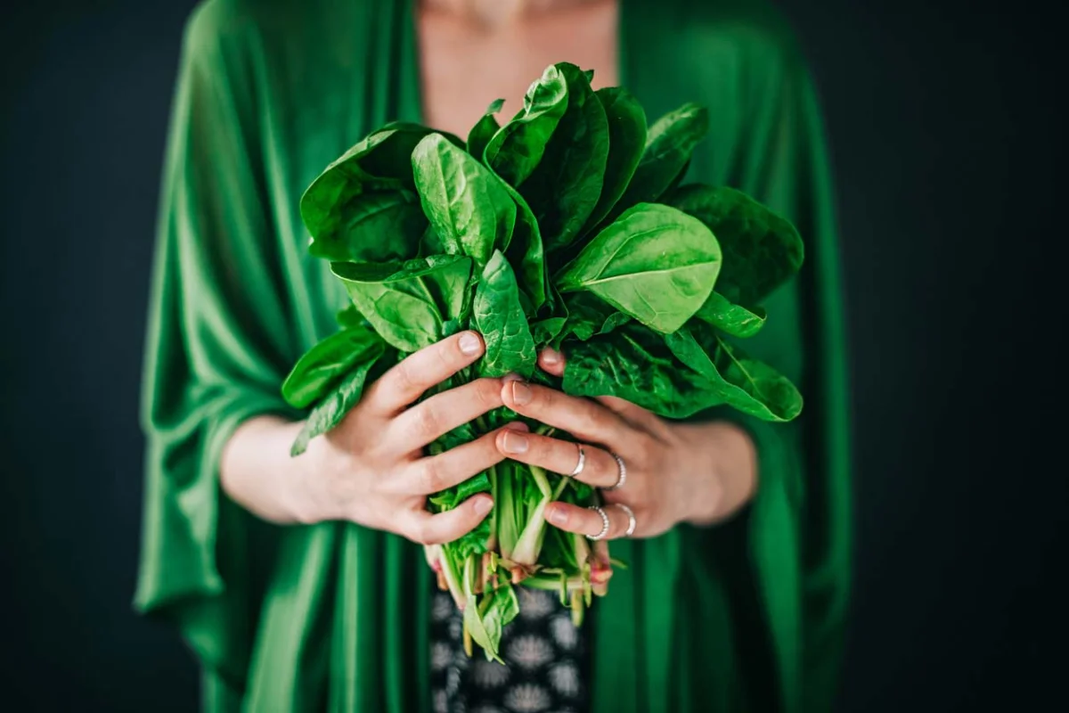 woman in green shirt holding freshly picked spinach