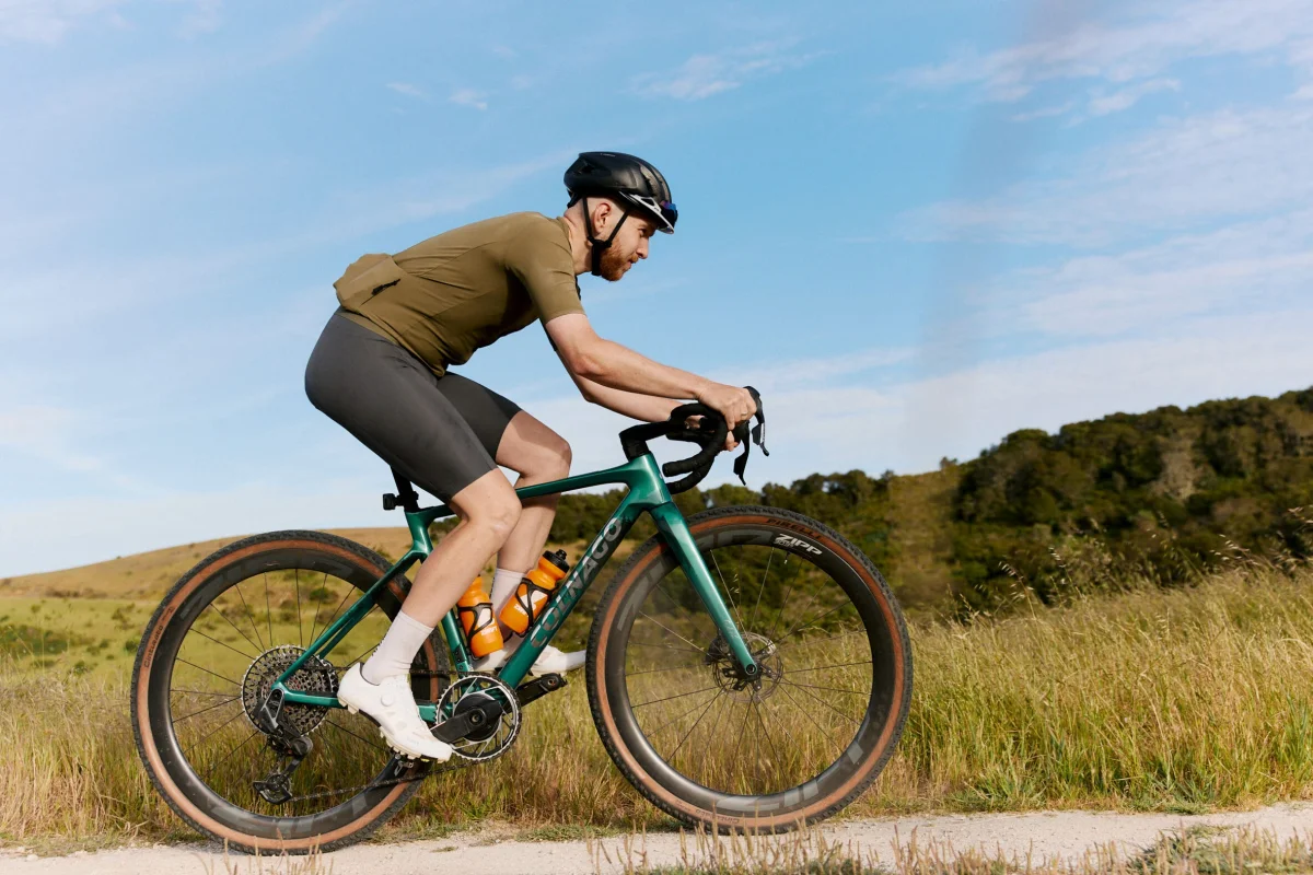 A cyclist wearing a helmet riding a gravel bike on a sunny day through a grassy landscape.