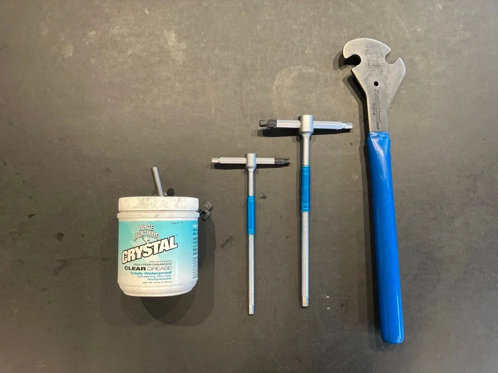 Assorted tools including grease, star and hex wrenches, and an adjustable wrench on a dark surface.