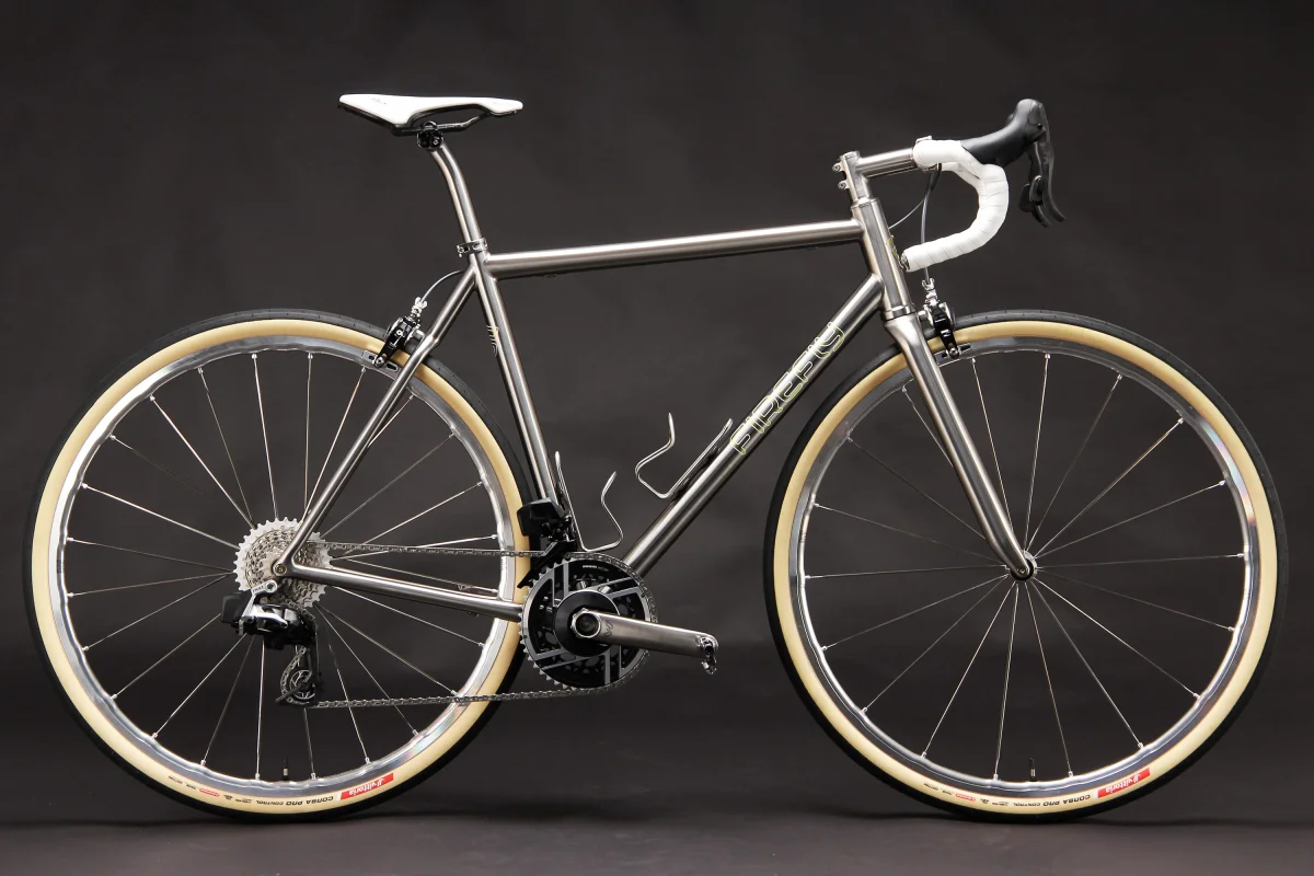 A sleek silver bicycle with drop handlebars and cream-colored tires on a dark background. A sleek silver bicycle with drop handlebars and cream-colored tires on a dark background.