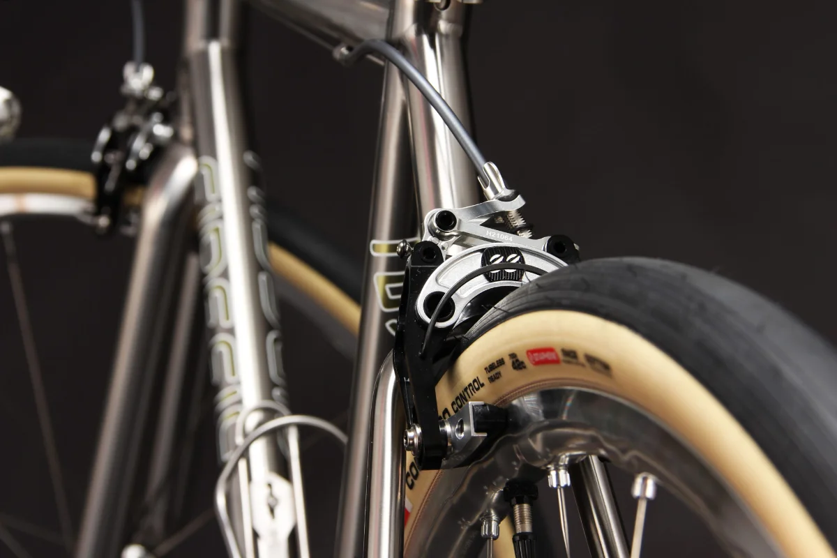 Close-up of a bicycle's brake system and wheel, showcasing metallic components and a tan tire. Close-up of a bicycle's brake system and wheel, showcasing metallic components and a tan tire.