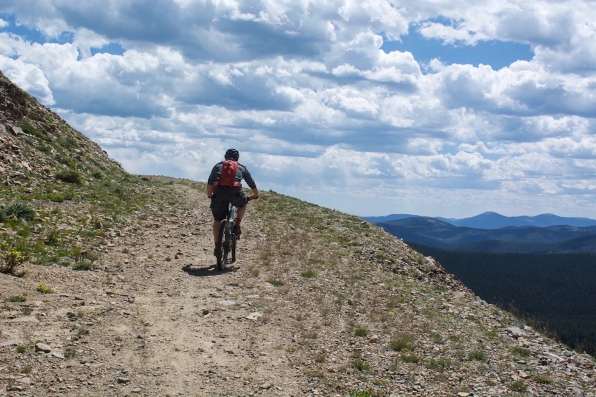 Mountain biker riding along a dirt trail with rocky terrain and expansive views under a cloudy sky. Mountain biker riding along a dirt trail with rocky terrain and expansive views under a cloudy sky.