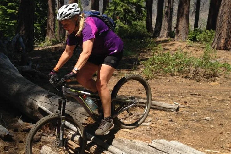 women riding mountain bike over logs women riding mountain bike over logs